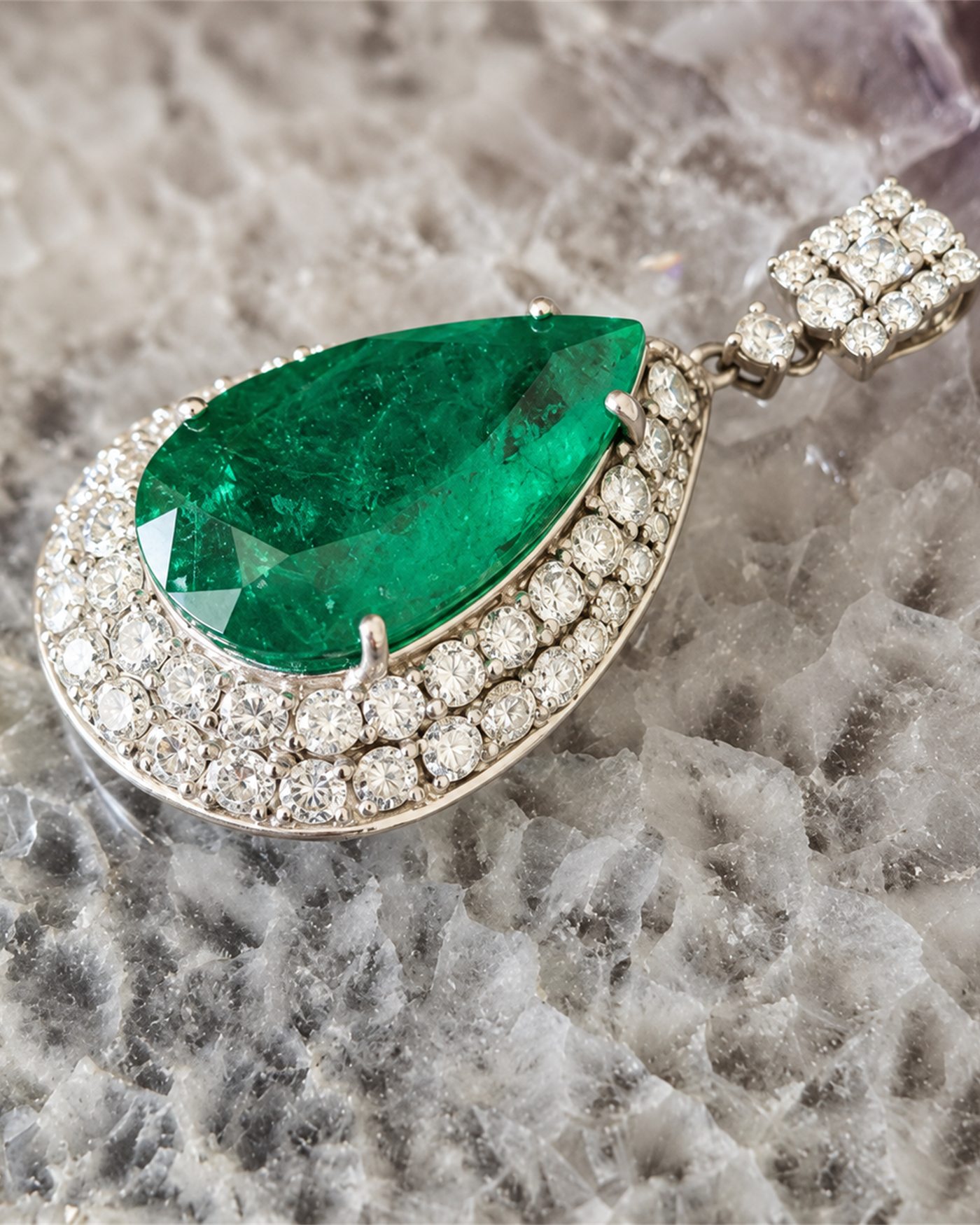 Pear-cut emerald pendant framed by a double diamond halo, resting on white coral