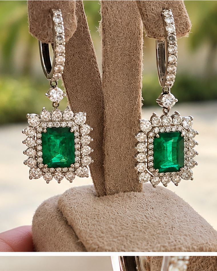 Emerald-cut emerald earrings in cushion diamond halos, shown on a display stand